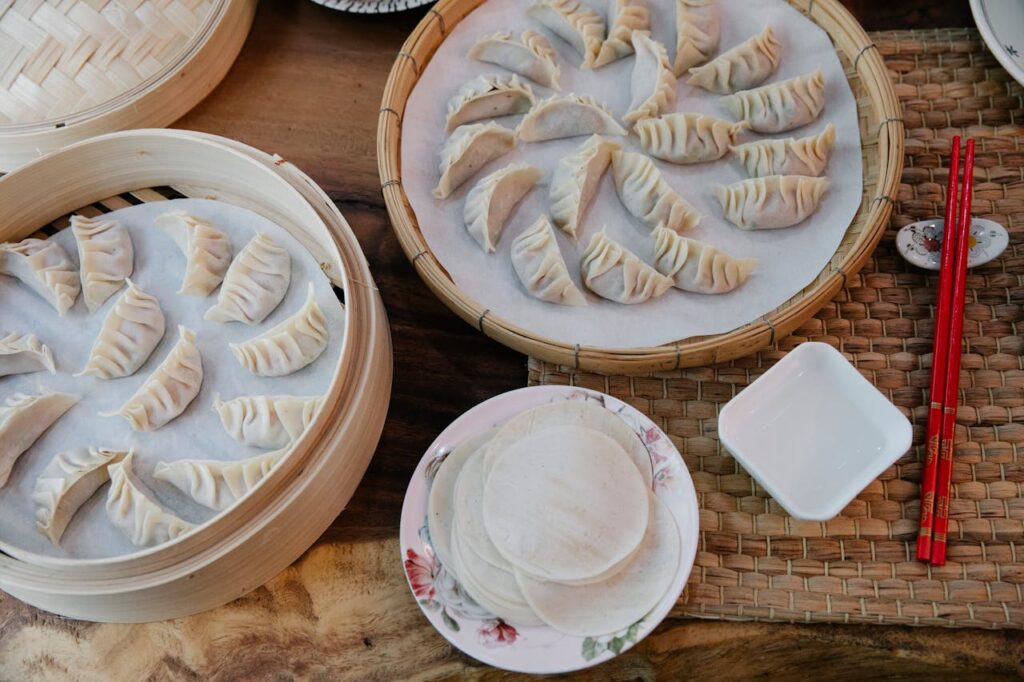 pexels-photo-7363671 A top view of freshly made dumplings in bamboo steamers with chopsticks, ready to be cooked.